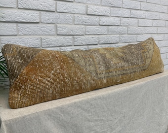 May include: A long, rectangular lumbar pillow featuring a woven textile cover with a distressed, vintage-inspired pattern in shades of mustard yellow, brown, and cream. The fabric displays a textured, knotted appearance with geometric motifs.