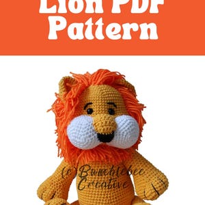 Peut inclure: Un jouet en peluche lion crocheté avec une crinière et une queue orange, un corps jaune, un museau blanc et des yeux noirs. Le jouet est assis sur un fond blanc. Le texte "(c) Bumblebee Creative" est visible sur le jouet.