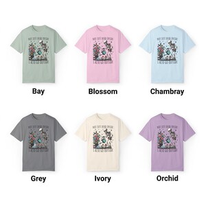 Pode incluir: Seis t-shirts de diferentes cores com um esqueleto a regar uma planta e o texto "Not just dead inside I also go outside". As cores s&atilde;o ba&iacute;a, flor, chambray, cinza, marfim e orqu&iacute;dea.