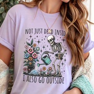 Pode incluir: Uma camiseta roxa com um esqueleto regando um vaso de flores. O texto na camiseta diz "Not just dead inside I also go outside".