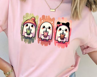 Pode incluir: T-shirt rosa claro com três fantasmas de desenho animado, cada um segurando um bubble tea. Um fantasma usa um gorro, outro um laço, e o terceiro está sem chapéu. Os fantasmas estão em fundos coloridos e abstratos.