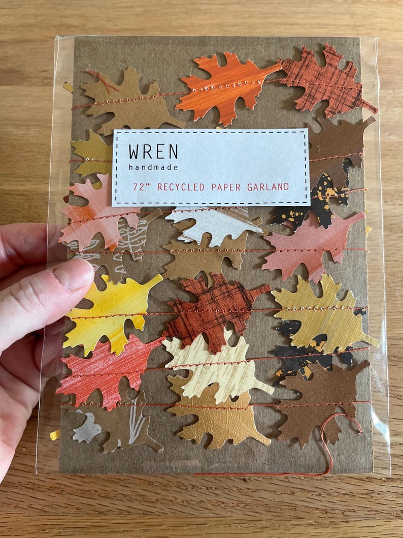 K&ouml;nnte beinhalten: Eine 183 cm lange Girlande aus recyceltem Papier mit bunten Herbstbl&auml;ttern in Orange, Gelb, Braun und Creme. Die Bl&auml;tter sind mit rotem Faden aufgereiht. Die Verpackung tr&auml;gt den Text "wren handmade".