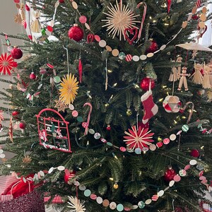 May include: A Christmas tree decorated with red and white paper ornaments, red and white candy canes, and straw stars. The tree is also decorated with a string of red, white, and green paper circles.