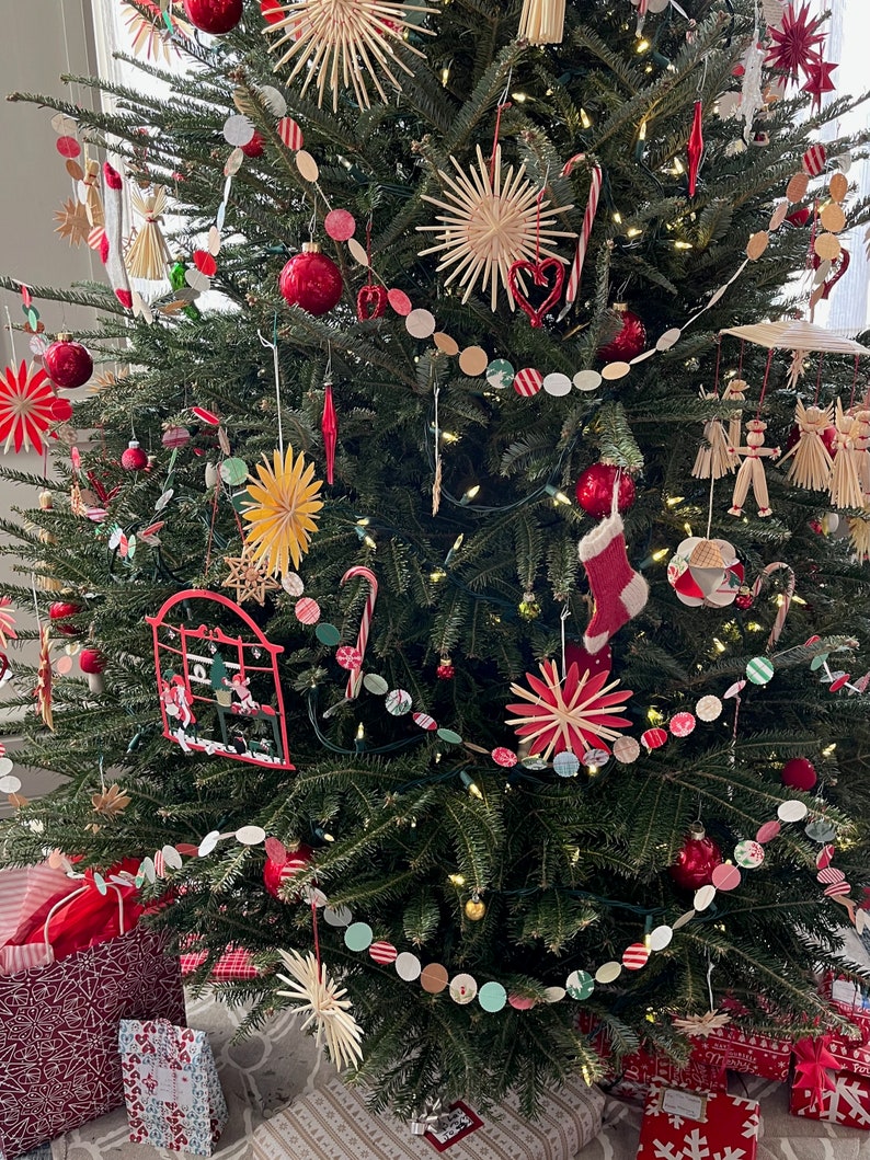 May include: A Christmas tree decorated with red and white paper ornaments, red and white candy canes, and straw stars. The tree is also decorated with a string of red, white, and green paper circles.