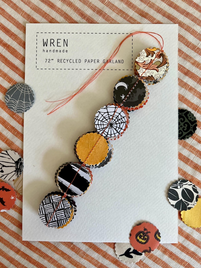 May include: A 72-inch recycled paper garland with various Halloween-themed designs, including a spiderweb, bats, and pumpkins. The garland is handmade and features a variety of colors and patterns. The card reads "wren handmade".