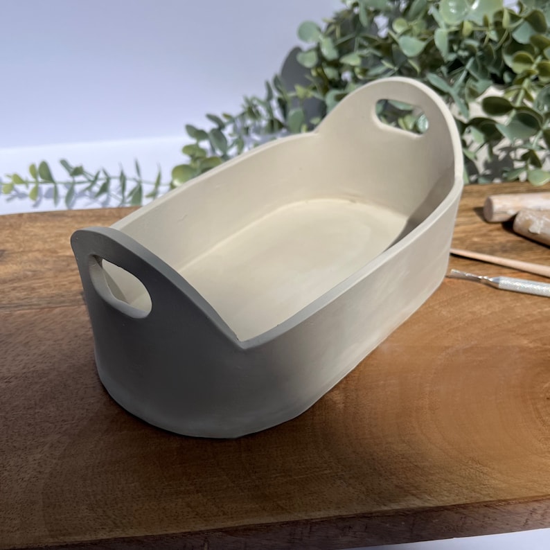 Puede incluir: Una bandeja peque&ntilde;a de cer&aacute;mica de forma ovalada con dos asas. La bandeja es de color beige claro y tiene un acabado liso y mate.