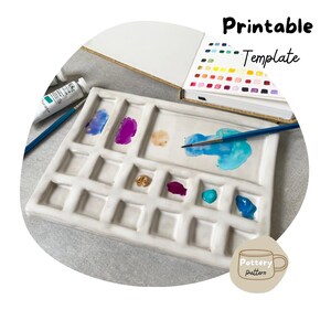 Puede incluir: Paleta de acuarela de cerámica blanca con 16 pocillos, un pincel y un tubo de pintura. La paleta está etiquetada como "Pottery pattern" y "Printable Template".