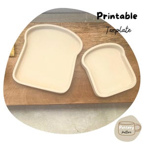 Peut inclure: Deux assiettes en céramique beige en forme de pain sur une surface en bois. La plus grande assiette est à gauche et la plus petite à droite. Les deux assiettes ont la forme d'une tranche de pain. Le texte "Modèle imprimable" est dans le coin supérieur droit de l'image.