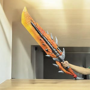 May include: A large, orange and black sword with a detailed design. The sword has a sharp point and a curved blade. The handle is black and has a textured grip.