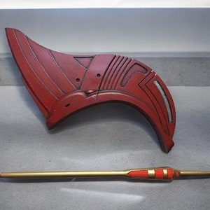 May include: A red and silver plastic prop resembling a helmet with a long, thin, gold-colored rod with red accents.