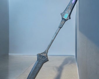 May include: A silver-colored spear with a textured surface and three gemstones embedded in the handle. The gemstones are purple, turquoise, and blue.