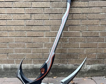May include: A silver and black metal hook with a red accent. The hook is curved and has a sharp point at the end. It is lying on a concrete surface with some leaves scattered around it.