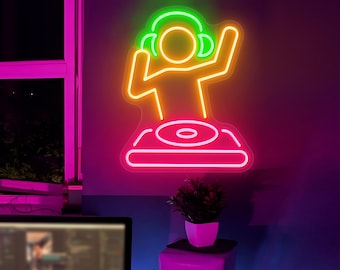 Può includere: Un'insegna al neon raffigurante un DJ con cuffie e braccia alzate, in piedi dietro una consolle. L'insegna è delineata in colori vivaci: verde per le cuffie, arancione per la figura e rosa per la base della consolle. Montata su un muro viola scuro.