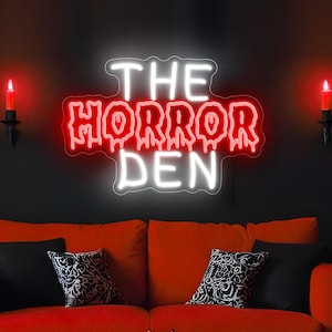 Könnte beinhalten: Ein Neonschild an einer dunklen Wand mit dem Schriftzug THE HORROR DEN in einer stilisierten Schriftart. Die Wörter THE und DEN leuchten in hellem Weiß, während das Wort HORROR in Rot gehalten ist und einen tropfenden Effekt aufweist.
