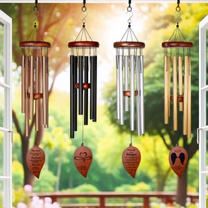 May include: Four wind chimes hanging from a hook. Each chime has a wooden top and a series of metal tubes in different colors: copper, black, silver, and gold. Each chime has a decorative leaf-shaped pendant with text.