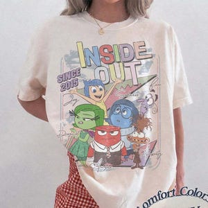 Peut inclure: T-shirt ivoire avec l'inscription "INSIDE OUT" et des personnages de dessins animés du film. Le t-shirt comporte également le texte "SINCE 2015" et le logo Comfort Colors. Il est porté avec un short à carreaux rouges et blancs.