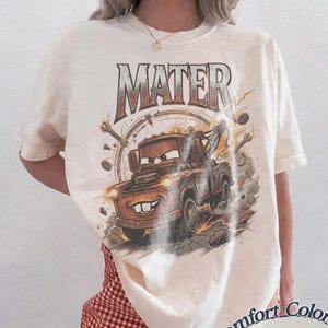 Puede incluir: Camiseta de color marfil con un gr&aacute;fico del personaje Mater de la pel&iacute;cula Cars. El dise&ntilde;o incluye la palabra "MATER" en una fuente desgastada sobre el personaje. La camiseta es de la marca Comfort Colors.