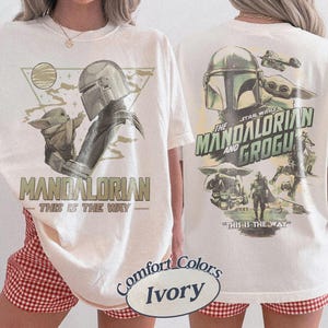 Op de afbeelding: Ivoor kleurig t-shirt met een afbeelding van The Mandalorian en Grogu. De voorkant toont "MANDALORIAN" en "THIS IS THE WAY." De achterkant toont "THE STAR WARS MANDALORIAN AND GROGU" met extra afbeeldingen.