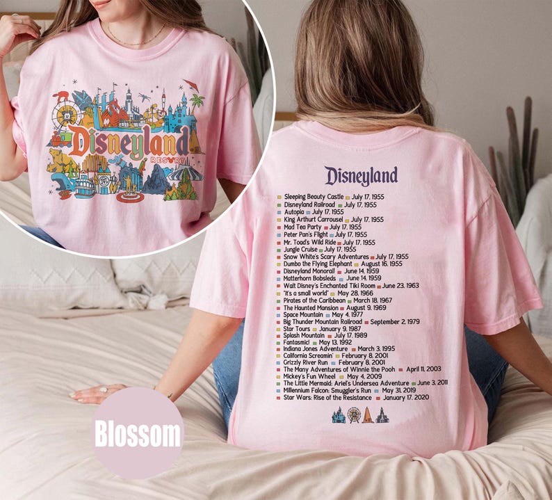 Puede incluir: Una camiseta rosa claro de Disneyland con un gr&aacute;fico colorido en la parte delantera y una lista de atracciones y fechas en la parte trasera. El gr&aacute;fico frontal presenta el logotipo de Disneyland y varios iconos del parque.
