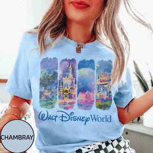 May include: Light blue t-shirt featuring a colorful graphic of Walt Disney World landmarks. The design includes illustrations of a castle, fireworks, and other park elements, with the words "Walt Disney World" in blue script.