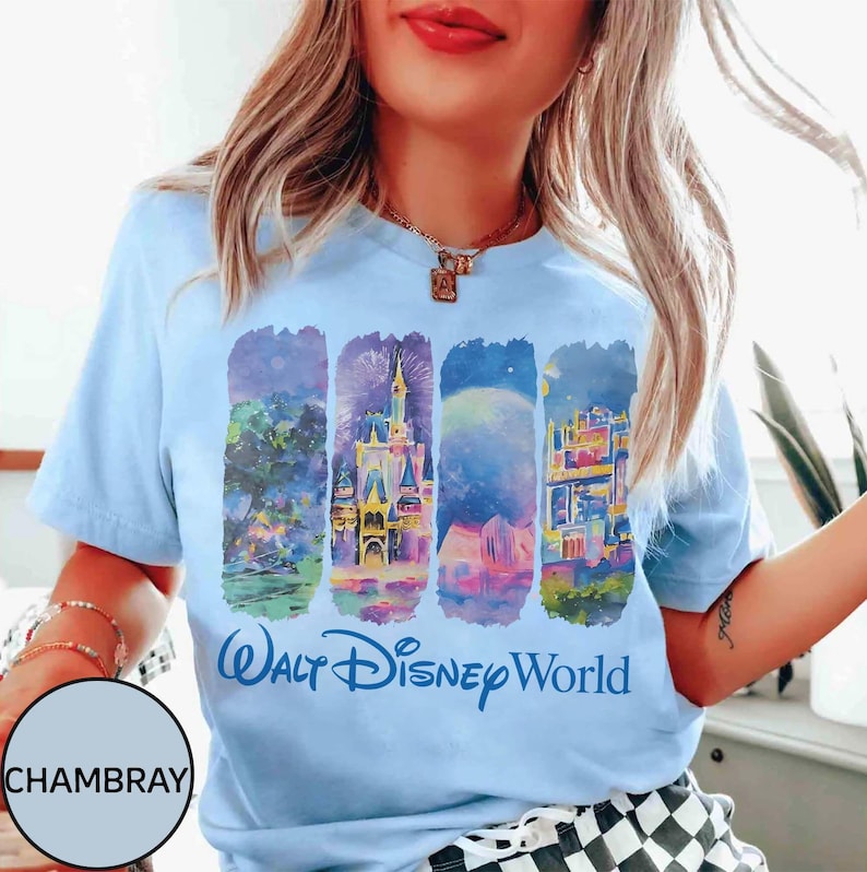 May include: Light blue t-shirt featuring a colorful graphic of Walt Disney World landmarks. The design includes illustrations of a castle, fireworks, and other park elements, with the words "Walt Disney World" in blue script.
