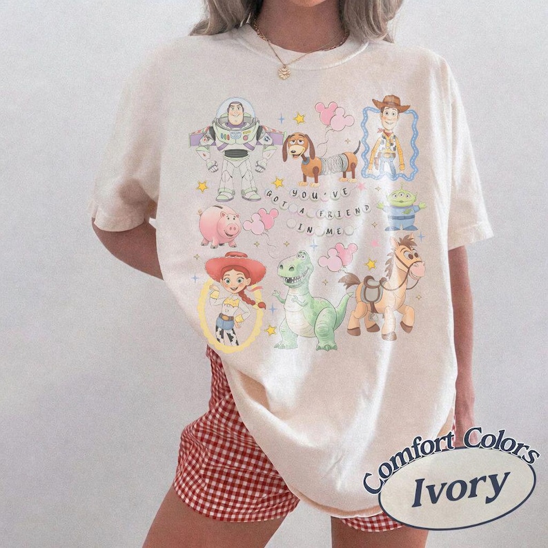 K&ouml;nnte beinhalten: Elfenbeinfarbenes T-Shirt mit bunten Zeichentrickfiguren aus dem Film Toy Story. Das Shirt zeigt Buzz Lightyear, Woody, Jessie, Rex und andere Charaktere. Der Text "YOU'VE GOT A FRIEND IN ME" ist ebenfalls auf dem Shirt aufgedruckt.