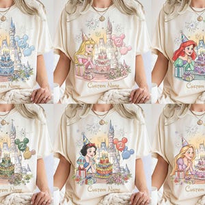 May include: Cream-coloured t-shirts featuring Disney princesses with birthday cake designs, castles, and the number 2. Each shirt includes the text "Custom Name" below the image, with a variety of princess illustrations.