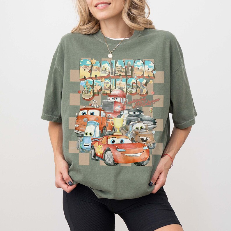 Peut inclure: T-shirt vert sauge avec un motif color&eacute; des personnages du film Cars et le texte "Radiator Springs". Le design comprend un motif &agrave; carreaux et divers v&eacute;hicules anim&eacute;s, id&eacute;al pour les fans.