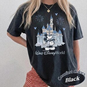 May include: Black t-shirt with a graphic of Cinderella's castle and Mickey Mouse. The words "Walt Disney World" are printed below the castle. The shirt also has the words "Comfort Colors Black" printed on it.