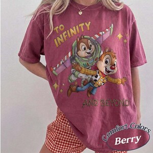 Puede incluir: Camiseta de color bayas con un gr&aacute;fico de Chip y Chop como Buzz Lightyear y Woody con el texto "TO INFINITY AND BEYOND". La camiseta tambi&eacute;n tiene las palabras "Comfort Colors" y "Berry".