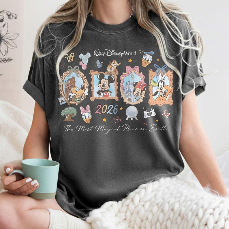May include: Dark gray t-shirt featuring a Walt Disney World design. The shirt includes framed images of Disney characters, the year 2026, and the phrase "The Most Magical Place on Earth."