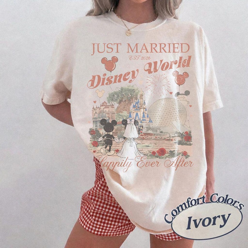 Pu&ograve; includere: T-shirt color avorio con tema matrimonio a Disney World. La maglietta presenta la scritta "Just Married Disney World Est 2026" con Topolino e Minnie, un castello e fuochi d'artificio. La maglietta &egrave; del marchio Comfort Colors.