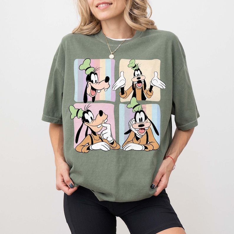 Może przedstawiać: Oliwkowo-zielona koszulka z czteropanelową grafiką Goofy'ego w r&oacute;żnych pozach. Każdy panel ma inne pastelowe tło. Goofy ma na sobie charakterystyczny zielony kapelusz i pomarańczową koszulę. Koszulka jest w stylu casual.