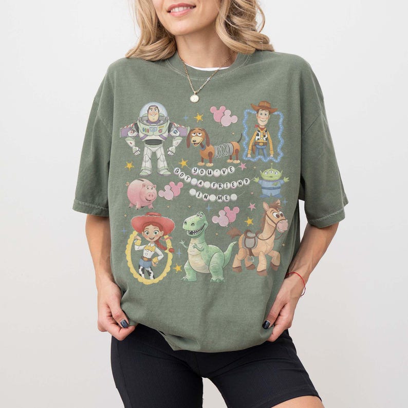 K&ouml;nnte beinhalten: Salbeigr&uuml;nes T-Shirt mit Cartoon-Figuren wie Buzz Lightyear, Woody und Jessie. Der Schriftzug "You've Got a Friend in Me" ist aufgedruckt. Das T-Shirt hat eine lockere Passform.