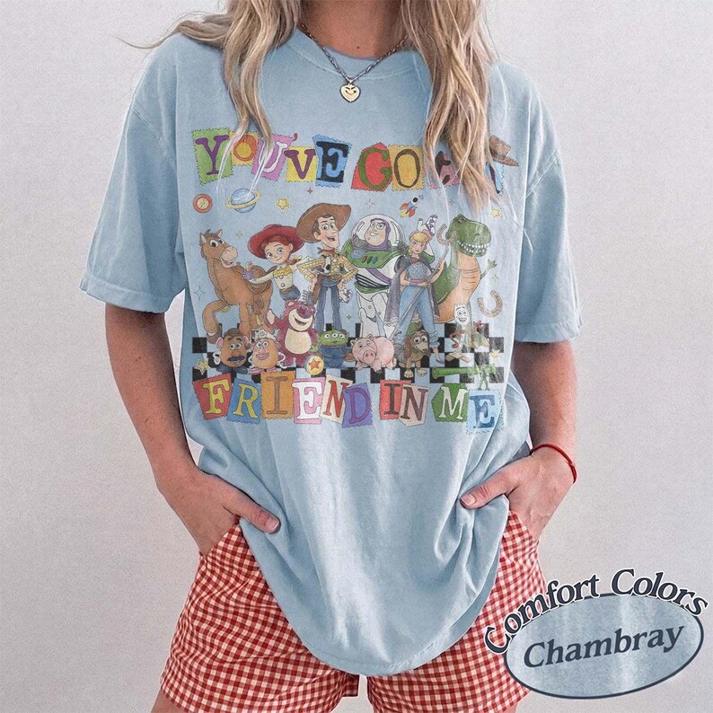 May include: A light blue short-sleeve t-shirt featuring a graphic print of various animated characters from the Toy Story franchise. The text "YOU'VE GOT A FRIEND IN ME" is printed in colorful, blocky letters above and below the character group.