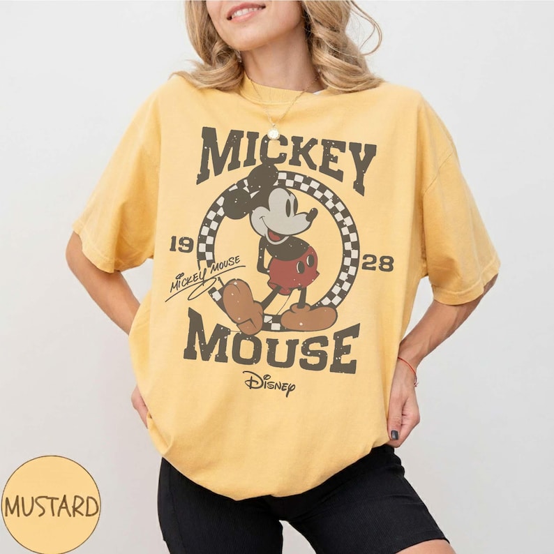 May include: Mustard yellow t-shirt featuring a vintage Mickey Mouse graphic. The design includes Mickey Mouse, the text "Mickey Mouse", and the years "1928" and "19". The shirt is a relaxed fit.