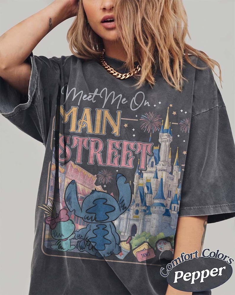 May include: Dark gray t-shirt with a graphic featuring Stitch from Lilo & Stitch, the text "Meet Me On Main Street", and a castle illustration. The shirt is labeled "Comfort Colors Pepper".