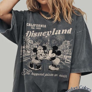 Puede incluir: Camiseta gris oscuro con un gr&aacute;fico desgastado de Disneyland. El dise&ntilde;o presenta a Mickey y Minnie Mouse, fuegos artificiales y el texto "California Est. 1955 Disneyland The happiest place on earth." La camiseta est&aacute; etiquetada como "Comfort Colors Pepper."