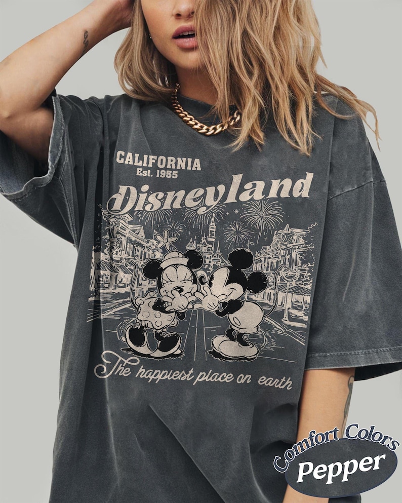 Puede incluir: Camiseta gris oscuro con un gr&aacute;fico desgastado de Disneyland. El dise&ntilde;o presenta a Mickey y Minnie Mouse, fuegos artificiales y el texto "California Est. 1955 Disneyland The happiest place on earth." La camiseta est&aacute; etiquetada como "Comfort Colors Pepper."