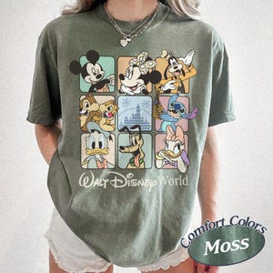 May include: Moss green t-shirt featuring a grid of Disney characters including Mickey Mouse, Minnie Mouse, Goofy, Chip and Dale, Stitch, Donald Duck, Pluto, and Daisy Duck. The words "Walt Disney World" are printed below the grid.