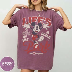 May include: Berry-colored t-shirt featuring Mickey Mouse with the text "Life's a Walk in the Park" and "Walt Disney World." The design includes a castle illustration. The shirt has short sleeves and a relaxed fit.