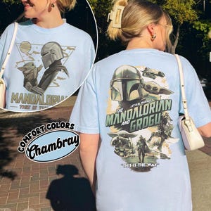 Op de afbeelding: Lichtblauw T-shirt met een afbeelding van The Mandalorian en Grogu uit Star Wars. Het ontwerp aan de voorkant bevat de tekst "MANDALORIAN" en "THIS IS THE WAY". Het ontwerp aan de achterkant bevat de tekst "STAR WARS THE MANDALORIAN AND GROGU".