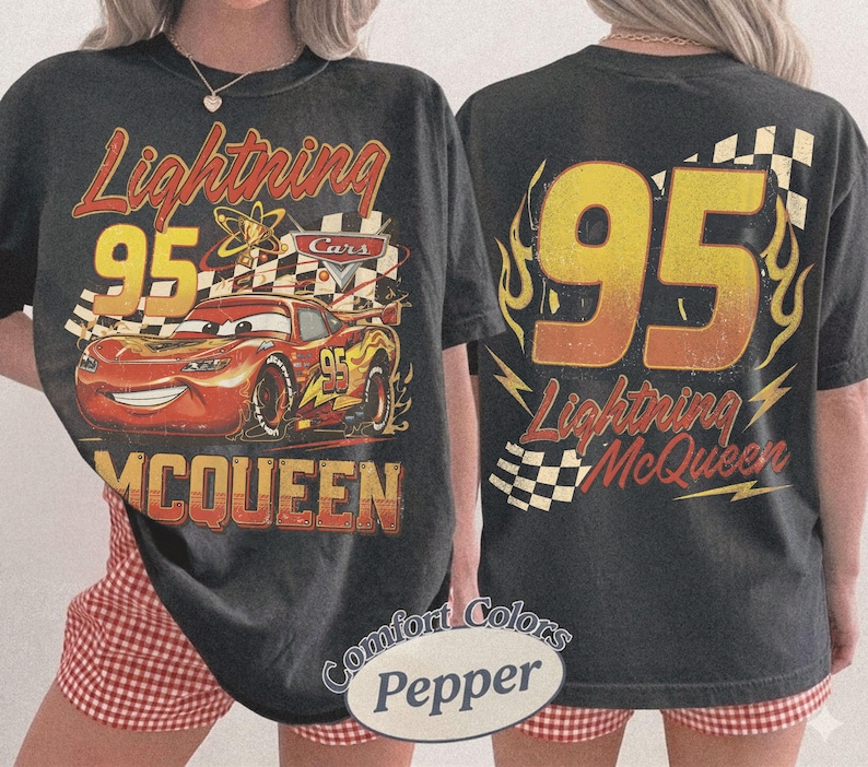 Może przedstawiać: Ciemnoszara koszulka z Lightning McQueen z filmu Auta. Prz&oacute;d przedstawia McQueena z numerem 95, flagą w szachownicę i napisem "Lightning McQueen". Tył ma duży numer 95 z płomieniami i "Lightning McQueen".
