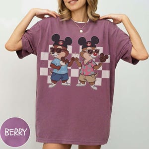 May include: Berry-colored t-shirt featuring a cartoon illustration of two chipmunks wearing sunglasses and Mickey Mouse hats, holding ice cream treats. The design is set against a checkered background. The word "BERRY" is printed on a circular label.