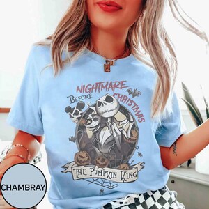 May include: Light blue t-shirt featuring a graphic from "The Nightmare Before Christmas." The design includes Jack Skellington, pumpkins, and the text "Nightmare Before Christmas" and "The Pumpkin King."