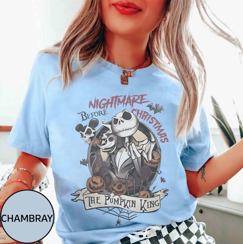 May include: Light blue t-shirt featuring a graphic from "The Nightmare Before Christmas." The design includes Jack Skellington, pumpkins, and the text "Nightmare Before Christmas" and "The Pumpkin King."