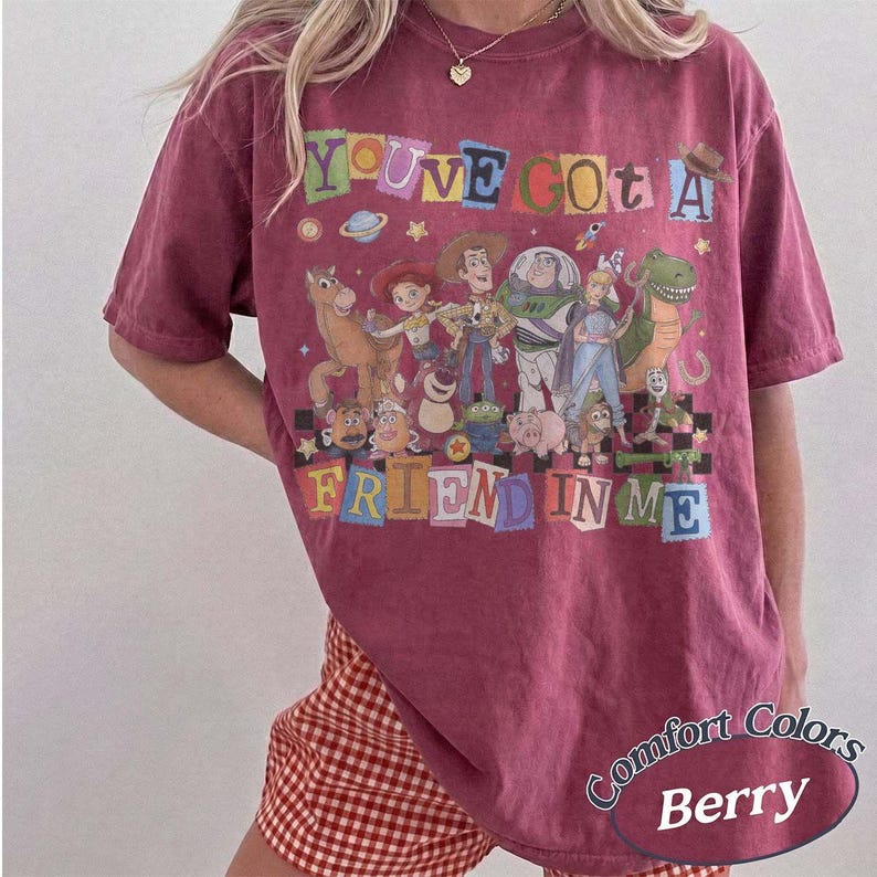 May include: A berry-colored short-sleeve t-shirt featuring a graphic print of various animated characters from the Toy Story franchise. The text "YOU'VE GOT A FRIEND IN ME" is printed in colorful, block-style letters above and below the characters.