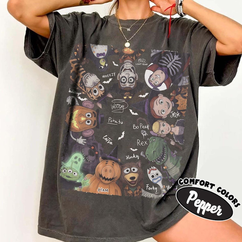 May include: A charcoal gray short-sleeve t-shirt featuring a graphic print of various animated characters in Halloween costumes. The design includes labels such as Woody, Buzz Lightyear, Jessie, Bo Peep, Rex, Forky, Ham, Lotso, Potato, and Wheezy.