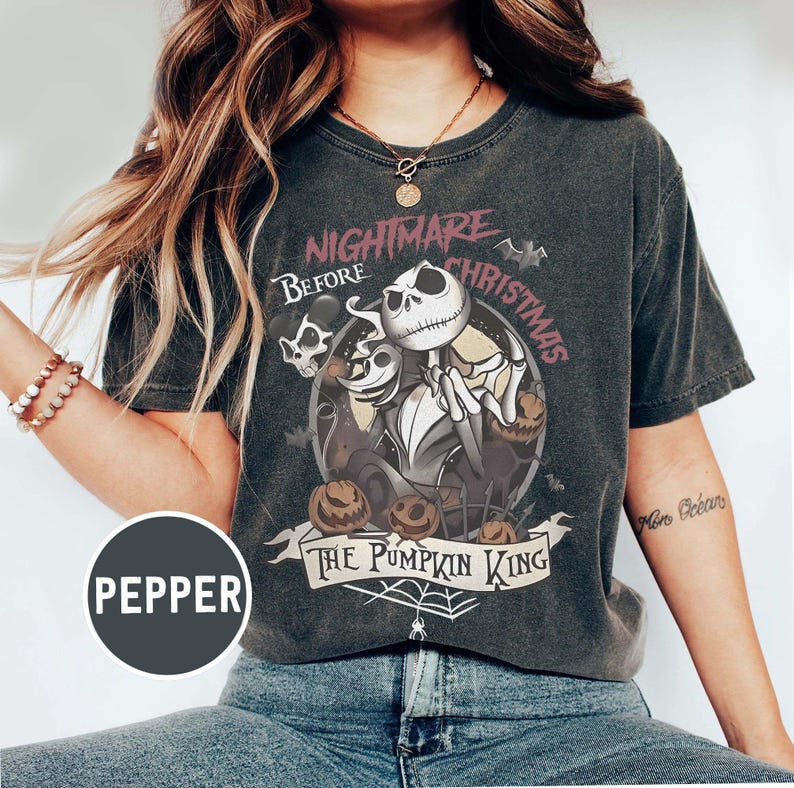 May include: Dark gray t-shirt featuring a graphic from "The Nightmare Before Christmas." The design includes Jack Skellington, pumpkins, and the text "The Pumpkin King." The shirt has a vintage, worn look.