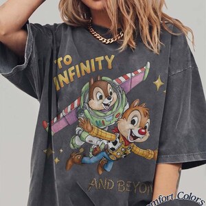 Puede incluir: Camiseta gris oscuro con Chip y Chop como Buzz Lightyear y Woody, con el texto "TO INFINITY AND BEYOND". La camiseta tiene un aspecto desgastado y el logo Comfort Colors Pepper.